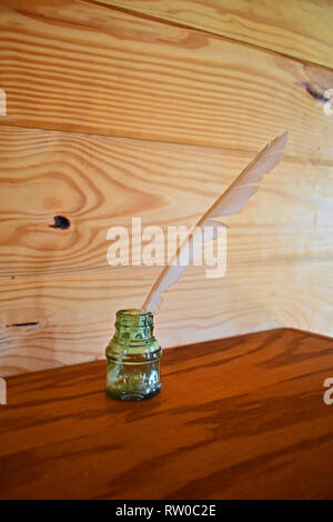 Antique glass inkwell with quill on wooden shelf with plain wooden background. Shingle Creek Pioneer Village, Kissimmee, Florida, USA. Stock Photo