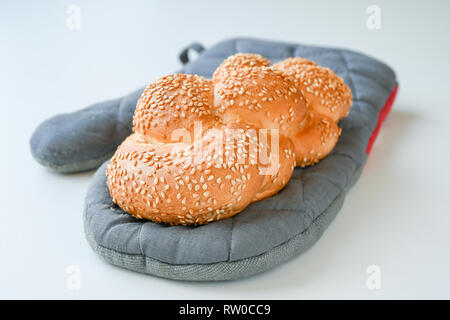Freshly baked brown sesame braid on a grey baking glove Stock Photo