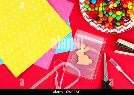 Diy Easter wrapping package sweets in a bag with a cut out bunny silhouette on a red background. Gift idea, decor Spring, Easter. Step by step. Top vi Stock Photo