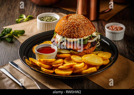 American burger with fried potatoes on the dark plate Stock Photo