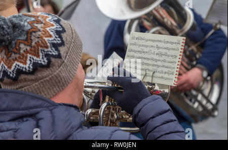 Playing a trumpet in a brass band at Christmas.  The man in a woolly hat is reading music while he plays Christmas carols in a brass band. Stock Photo