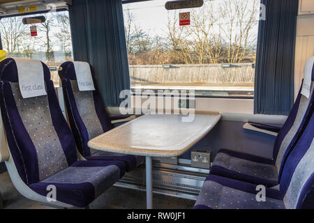 First class carriage sitting empty on a train.  The four blue seats and table are next to a window with a FIRST CLASS sign Stock Photo