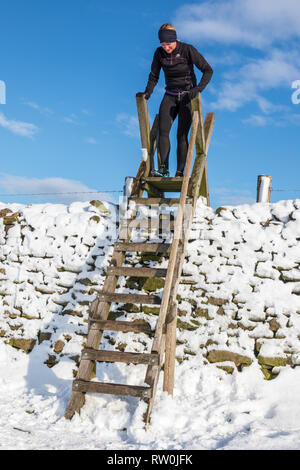 Snow covered dry stone wall in the Derbyshire Peak District,  Ladder style against a cold blue sky. Stock Photo