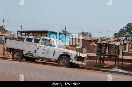 A old white car with flat tires parked at a road in Ghanaian town Bolgatanga, Ghana, West Africa Stock Photo