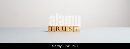 Wide view image of five wooden blocks with letters spelling the word Trust over grey background in a conceptual image. Stock Photo
