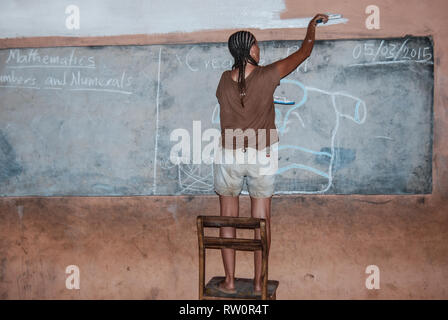 A woman with afro braids is painting a wall of a local elementary school in Ghana, Africa Stock Photo