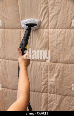 A woman cleaning linen blanket with stream cleaner. Stock Photo