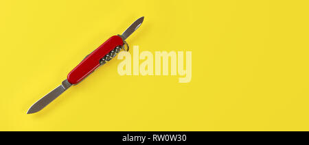 Table top view, red pocket knife with both blades opened, on yellow board. Space for text on right. Stock Photo