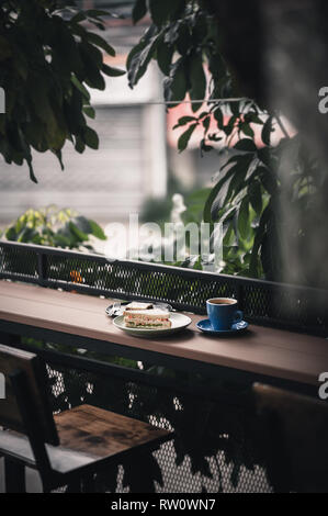 Abstract scene of breakfast meal set including tuna sandwich, hot long black coffee, and brownie cheese cake on outdoor wood bar. Weekend morning acti Stock Photo