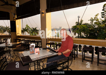 Cambodia, Phnom Penh, City Centre, Sisowath Quay, Foreign Correspondent’s Club FCC hotel restaurant, senior tourist reading breakfast menu Stock Photo