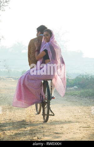 Rear view of a happy rural couple riding on bicycle in a village. Stock Photo