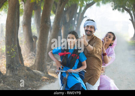 Happy rural couple along with their daughter riding on bicycle in village. Stock Photo