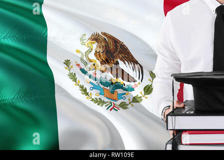 Successful Mexican student education concept. Holding books and graduation cap over Mexico flag background. Stock Photo