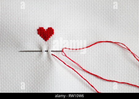 Hand-embroidered heart, needle, red thread, white canvas Stock Photo