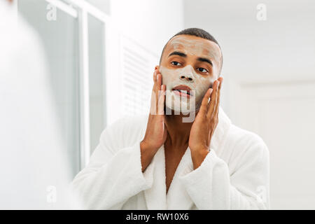 Portrait of a young man using a natural clay facial mask in bathroom Stock Photo