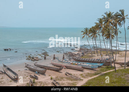 A landscape photo of the beautiful tropical coast and sandy beach at Elmina, Ghana. Old traditional wooden fishing boats are stored at the beach. Stock Photo