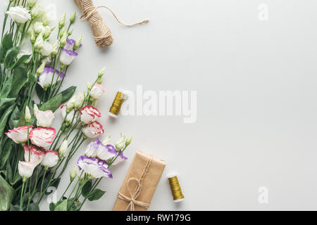 top view of eustoma, wrapped gift, twine and spools of thread on grey background Stock Photo