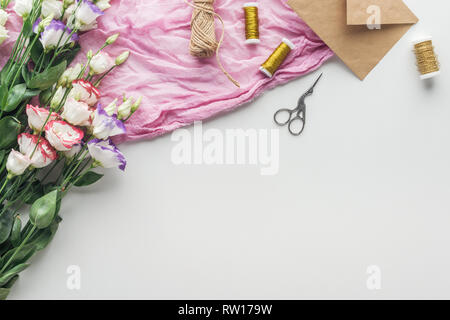 top view of eustoma, envelopes, spools of thread, scissors and cloth on grey background Stock Photo