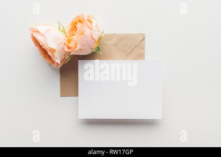 top view of empty blank over brown envelope and pink roses on grey background Stock Photo