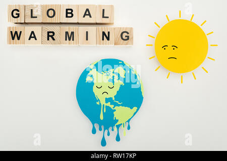 paper cut melting earth and sun with sad face expressions, thermometer with high temperature on scale, and 'global warming' lettering on wooden cubes  Stock Photo