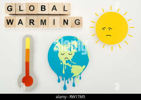 paper cuts melting earth and sun with sad face expressions, thermometer, and wooden cubes with 'global warming' lettering on grey background Stock Photo