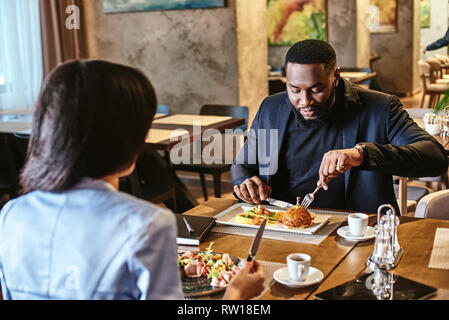Portrait of co-workers having business lunch at restaurant, sitting at table, discussing project while eating salad and chicken leg. Stock Photo