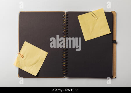 top view of opened notebook with black sheets and sticky notes with paper clips on white background Stock Photo
