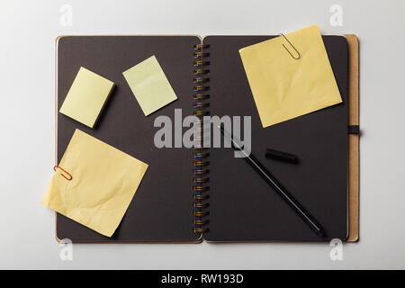 top view of opened notebook with black sheets and yellow sticky notes with paper clips on white background Stock Photo