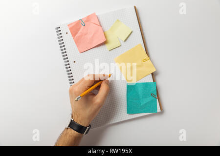cropped view of man writing on blank squared sheet near crumpled paper sticks on white background Stock Photo