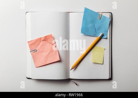 top view of opened notebook with sticky notes and paper clips near pencil on white background Stock Photo