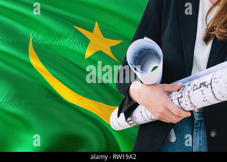 Mauritanian Architect woman holding blueprint against Mauritania waving flag background. Construction and architecture concept. Stock Photo