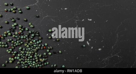 Tabletop view, Black pepper (Piper nigrum) spice spilled on dark marble like board. Turkish green / blue peppercorn variant. Banner with space for tex Stock Photo