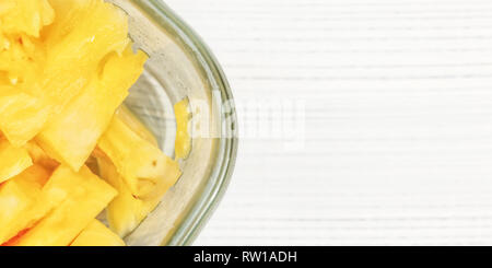 Tabletop view, detail - pieces of juicy pineapple in glass bowl on white boards desk. Stock Photo