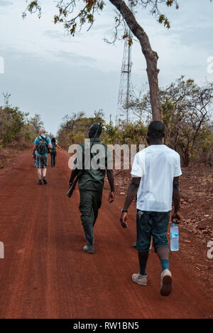 Tourists and an armed park ranger walking on a road at the Mole National Park, Ghana Stock Photo