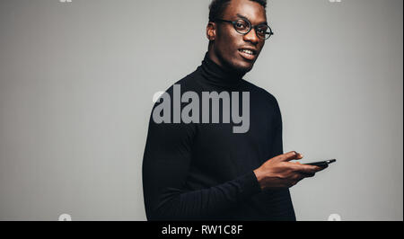 Portrait of handsome african man with a smart phone.  African guy looking at camera while using a mobile phone on gray background. Stock Photo