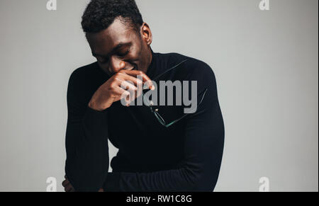 Young man with eyeglasses dreaming and smiling with closed eyes on gray background. African man in black t-shirt. Stock Photo