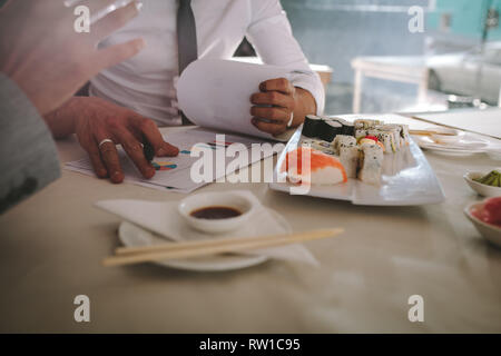 Food on table with business people discussing over statistical chart at restaurant. businessmen having a meeting during lunch at restaurant. Stock Photo