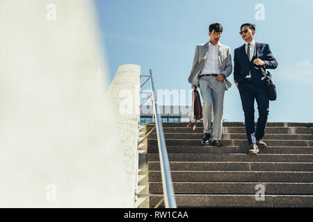 Two business people walking down stairs. Korean business men talking and walking down the steps. Stock Photo