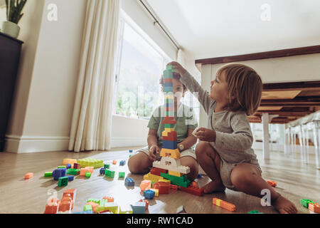 Kids making a tower using building blocks. Happy kids playing with toys sitting on floor at home. Stock Photo