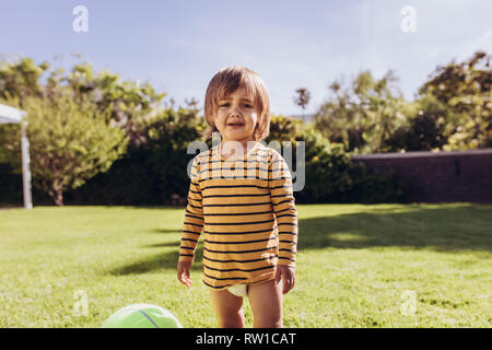 Portrait of a boy standing alone in park and crying. Little boy playing with ball in a park on a sunny day. Stock Photo