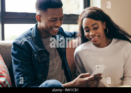 Students relaxing together in campus building. Young man and woman sitting at sofa looking at mobile phone. Stock Photo