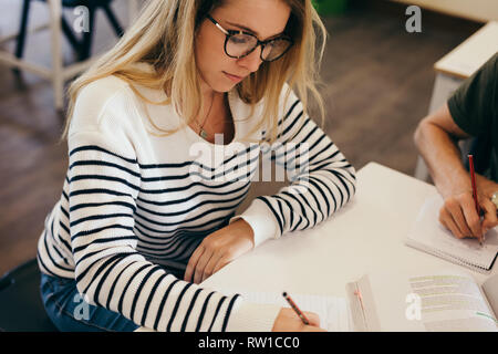 Girl writing in book with classmates sitting by. Female students studying with classmates. Stock Photo