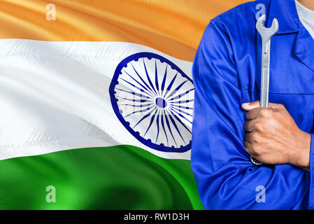 Indian Mechanic in blue uniform is holding wrench against waving India flag background. Crossed arms technician. Stock Photo