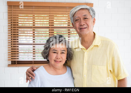 Asian senior couple embrace togerther and looking at camera in living room at home.Happy retirement lfie.aging at home concept Stock Photo