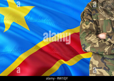 Crossed arms Congolese soldier with national waving flag on background - Congo Military theme. Stock Photo