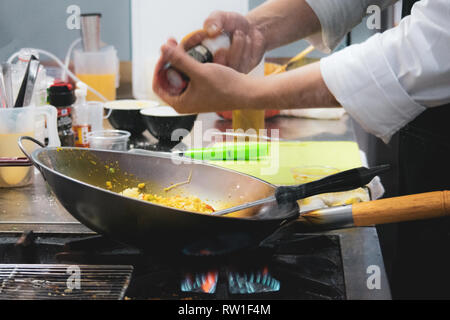 Chef cooking with flame in a frying pan on a kitchen stove, Chef in restaurant kitchen at stove with pan Stock Photo