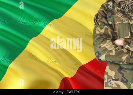 Crossed arms soldier with national waving flag on background - Republic Of The Congo Military theme. Stock Photo