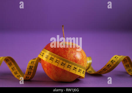 An apple wrapped into measuring tape, violet background, free copy space, selective focus Stock Photo