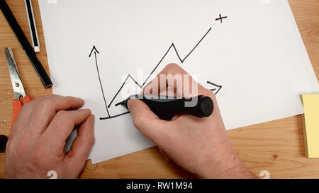 top view, a businessman's hand draws a graph that goes into positive value, footage ideal for topics such as economics, business, trade and analysis Stock Photo