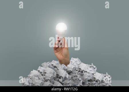The hand holding a light bulb emerges from the crumpled paper. Idea concept. Stock Photo